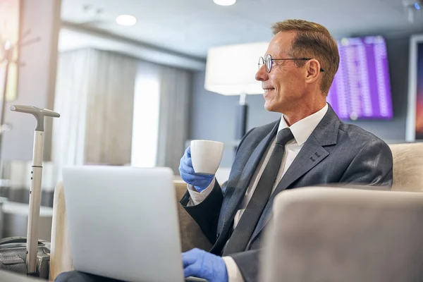 Merry mature businessman with laptop in airport lounge — Stock Photo, Image