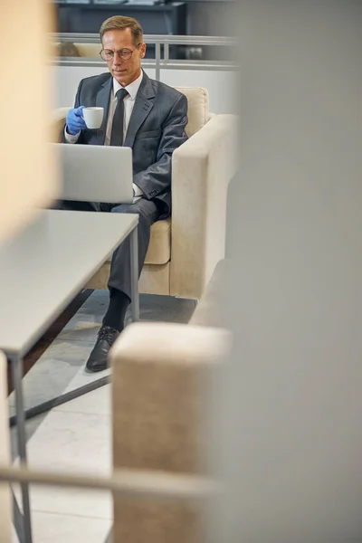 Elegant man with coffee and laptop in airport lounge