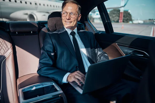 Wesoły biznesmen z laptopem w samochodzie na lotnisku — Zdjęcie stockowe