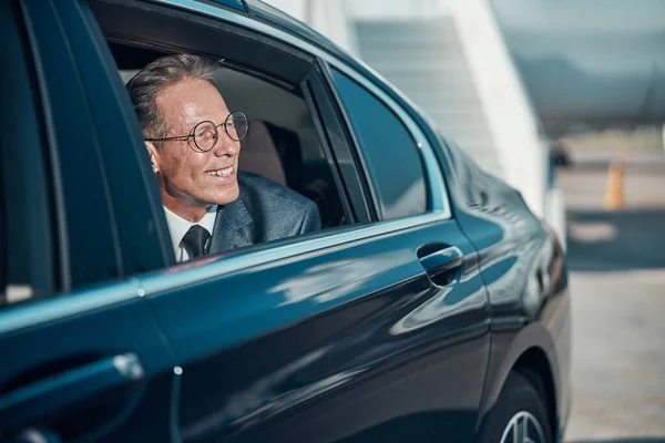 Hombre de negocios sonriente saliendo del aeropuerto en coche con conductor — Foto de Stock