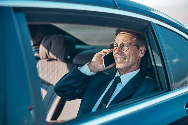 Cheerful businessman talking on smartphone during transfer from airport — Stock Photo, Image