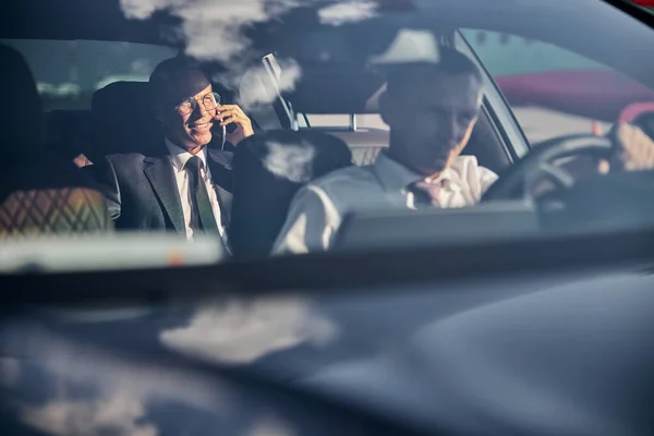 Hombre de negocios sonriente con smartphone viajando con chofer — Foto de Stock