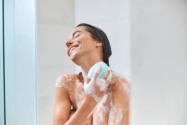 Glädjande ung kvinna som använder bad loofah när du tar dusch — Stockfoto