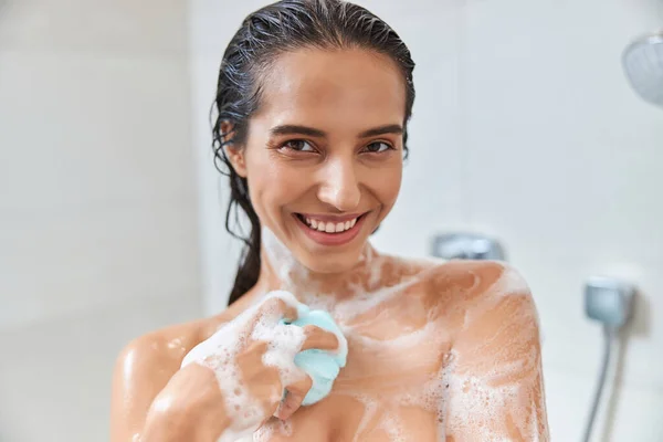 Jovem encantadora usando banho loofah enquanto toma banho — Fotografia de Stock