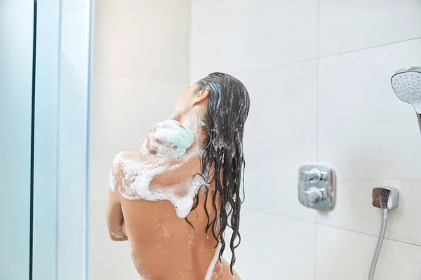 Brunette jonge vrouw wassen lichaam met douche loofah — Stockfoto