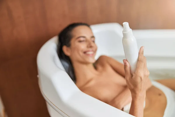 Joyeux jeune femme tenant bouteille de lotion tout en prenant un bain — Photo