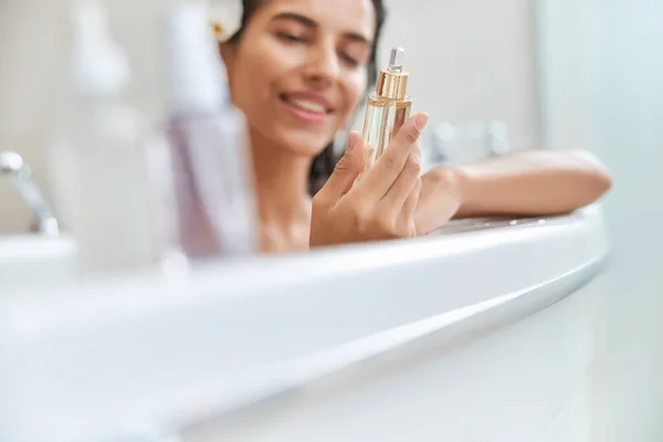 Usmívající se mladá žena drží láhev séra obličeje při koupeli — Stock fotografie