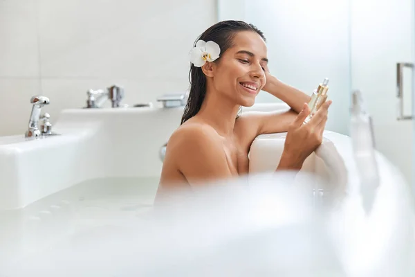 Hermosa mujer joven sosteniendo botella de suero facial mientras toma el baño — Foto de Stock