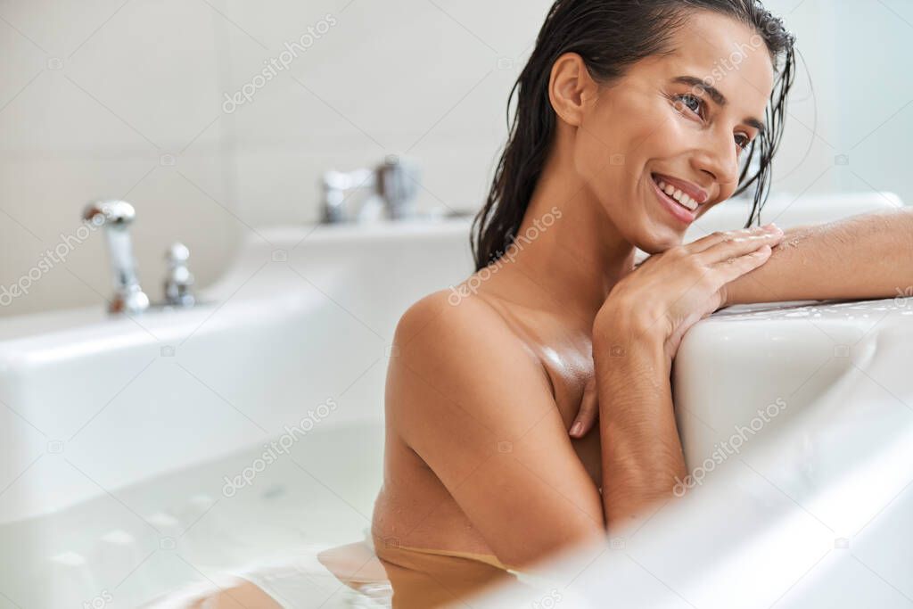 Beautiful young woman lying in white bathtub at home