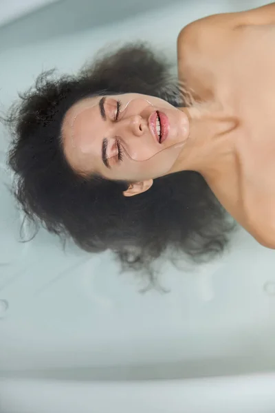 Attractive young woman lying in water in bathtub