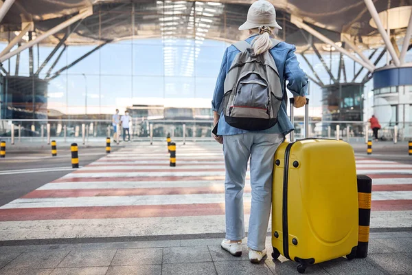 공항 건물을 바라보고 있는 카트 여행 가방을 든 여자 — 스톡 사진