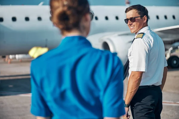 Veselý hezký pilot s letuškou kráčející k tryskáči — Stock fotografie