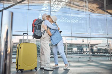 Cep telefonlu bir adam neşeli bir kadına sarılıyor.