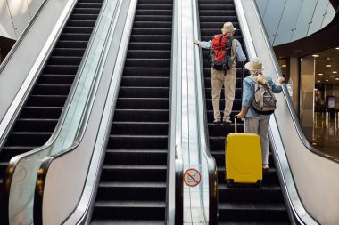 İki kıdemli turist hareket halindeki merdivenleri kullanıyor.