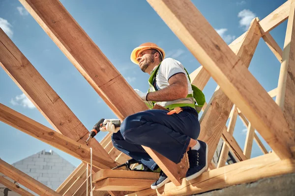 Construtor competente sentado no alto do feixe — Fotografia de Stock