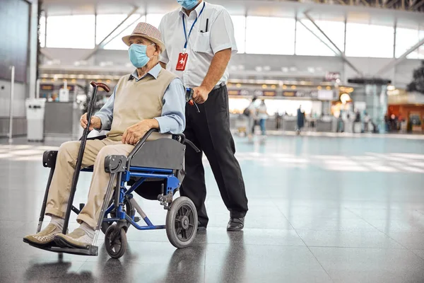 Trabalhador do aeroporto rolando uma cadeira de rodas com um homem idoso — Fotografia de Stock