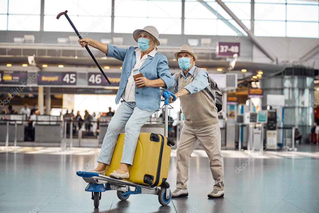 Male pensioner wheeling his wife on a baggage trolley