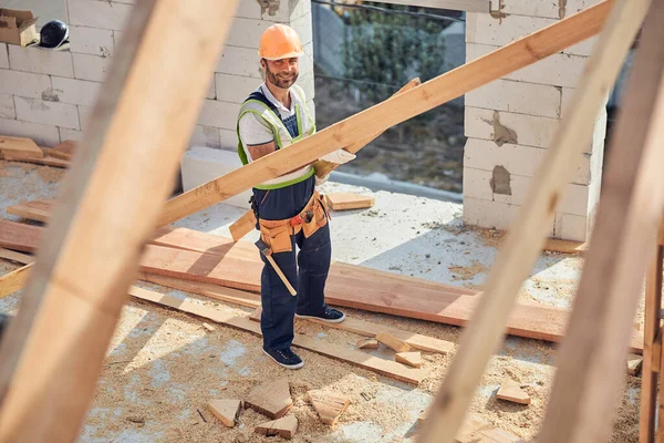 Trabalhador do canteiro de obras sorridente posando enquanto trabalhava com materiais de madeira — Fotografia de Stock
