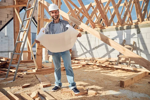 Jovem alegre com um chapéu duro segurando um plano de construção — Fotografia de Stock