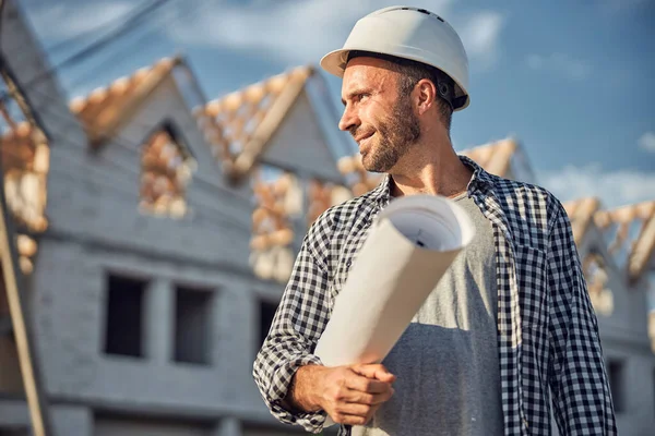 Arquiteto alegre que parece orgulhoso enquanto carrega um plano de construção — Fotografia de Stock