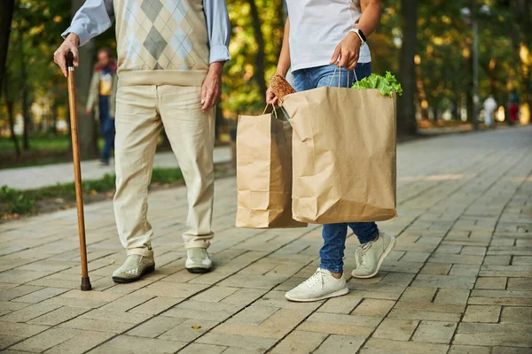 Mujer sosteniendo bolsas de papel en la mano cerca del anciano —  Fotos de Stock