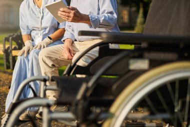 Yaşlı kadın ve erkek hekimin önünde tekerlekli sandalye.