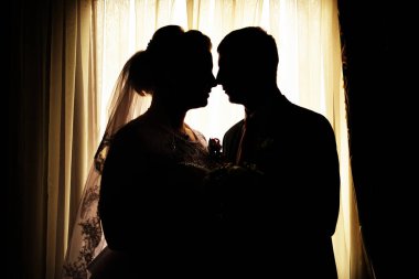 Yeni evlilerin karanlık siluetleri pencereye karşı arka planda.