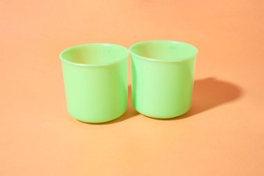 Turuncu arka planda iki açık yeşil plastik bardak var.               