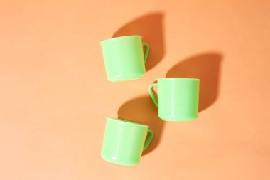 Turuncu arka planda üç açık yeşil plastik bardak var.