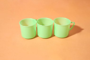 Turuncu arkaplana üç açık yeşil plastik bardak yerleştirilir.     