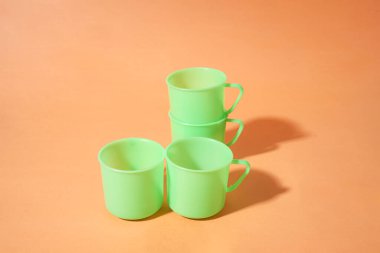 Turuncu arkaplana dört yeşil plastik bardak konur.                 