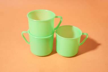 Turuncu arka planda üç açık yeşil plastik bardak sergilenir              