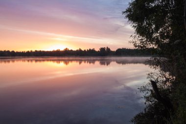 Orman gölünün üzerinde gün doğumu. Göldeki gökyüzünün yansıması. Yaz.