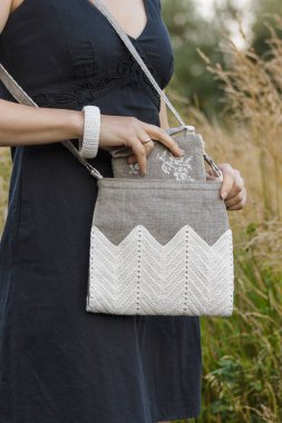 Crossbody bag in women's hands. Makeup bag and bracelet. Linen bag. Knitted white decor. clipart