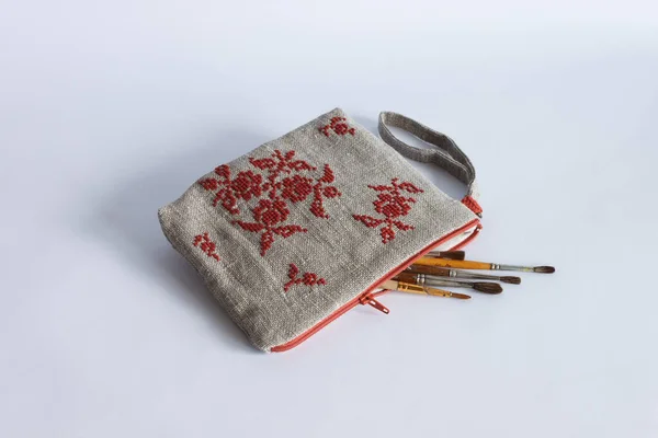 Makeup bag made from linen cloth and embroidered with red threads. Personalized wristlet bag. Light background.