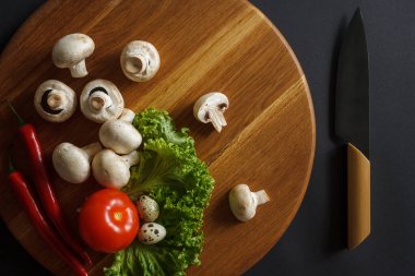 Sebze dolu bir hayat. İçinde şampiyonlar, yeşil salata, akut kırmızı biber ve mutfak bıçağı bulunan tahta bir tahta tahta tahta. Mutfak konsepti. Karanlık arka plan. Yukarıdan görüntüle.