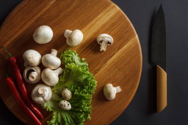 Sebze dolu bir hayat. İçinde şampiyonlar, yeşil salata, akut kırmızı biber ve mutfak bıçağı bulunan tahta bir tahta tahta tahta. Mutfak konsepti. Karanlık arka plan. Yukarıdan görüntüle.
