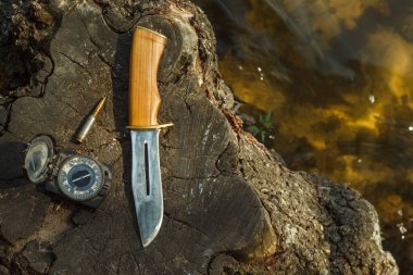 Av bıçağı, eski pusula ve şarjör 5.45 suyun yanındaki kütüğe yerleştiriliyor. Açık havada av malzemeleriyle dolu bir hayat. Yakın plan..