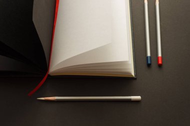 Eskiz defterini ve renkli kalemleri koyu bir arkaplanda aç. Hobi ve el işi konsepti. Üst görünüm.