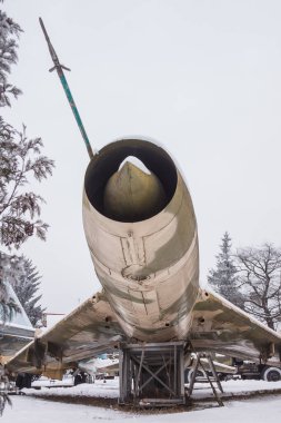 Eski jet uçağının arka planında askeri teçhizat karla kaplı.