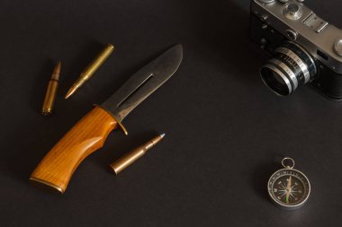 Avcı bıçağı, pusula, tüfek fişeği ve siyah arka planda eski analog film kamerası olan bir hayat. Yüzeyin derinliği (DOF)