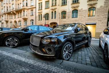 Prag, Çek Cumhuriyeti - 29 Ağustos 2025: Siyah Bentley Bentyaga off-road otomobili pahalı bir mağazanın önünde caddeye park edildi. Gün batımında jipleri ve lüks mağazaları olan akşam şehri..
