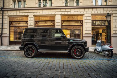 Prag, Çek Cumhuriyeti - 29 Ağustos 2025: Siyah Mercedes G off-road otomobili şehrin caddesine park edilmiş pahalı bir mağazanın önünde. Gün batımında SUV ve lüks mağazaları olan akşam şehri..