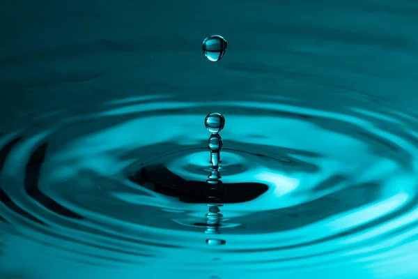 Perfect water drop splashing into smooth water causing ripples in a calm surface