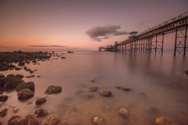Gün batımında Llandudno rıhtımında pürüzsüz bir deniz ve kayalarla