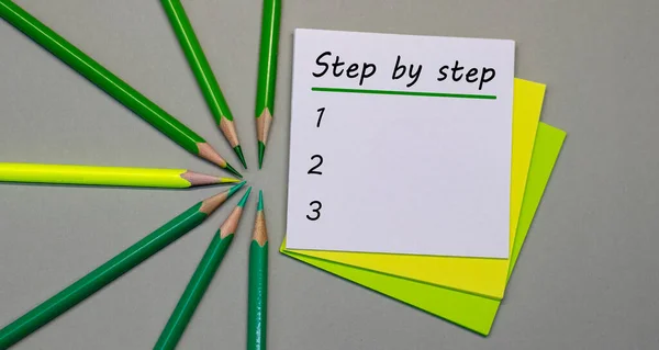 Yellow and green pencils laid out in a semicircle. Inscription on stickers - step by step. Background. Empty space