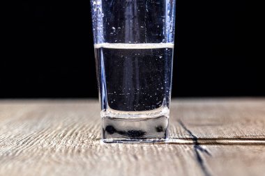 Siyah arka planı olan ahşap bir masanın üzerinde suyla dolu cam.