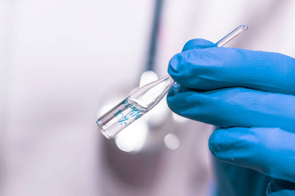 Close-up of a doctor's hand in a glove holds a glass ampoule with a medicine. Medicine and healthcare concept.