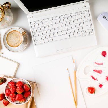 Düz yatıyordu trendy kadınsı ev sanat çalışma alanı. Ev ofis büro dizüstü bilgisayar, dizüstü bilgisayar, boyalar, fırçalar, tuval, taze çilek ve beyaz zemin üzerine kahve fincanı. Yaratıcı arka plan sanat