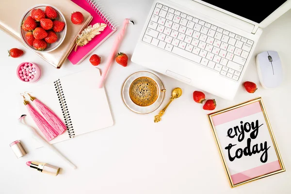 Trendy feminine home workplace. Home office desk with laptop, notebook, fresh strawberries, cosmetics, accessories and coffee cup on white background. Flat lay, top view
